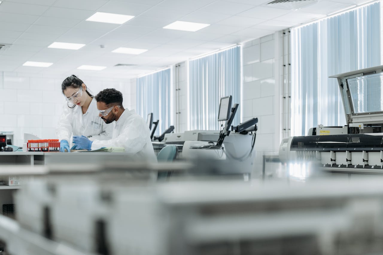 Two scientists working in a high-tech laboratory setting, wearing protective eyewear and gloves.